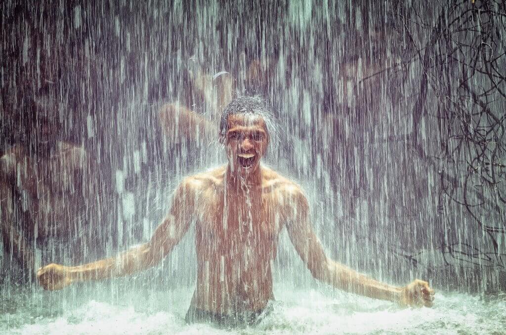 choosing the right lube for sex is can make it feel like you're playing in a waterfall like this man who is under a waterfall with a smile on his face